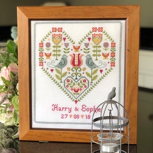 May include: A framed cross-stitch design featuring a heart with flowers, birds, and the text "Harry & Sophie 27 08 18".