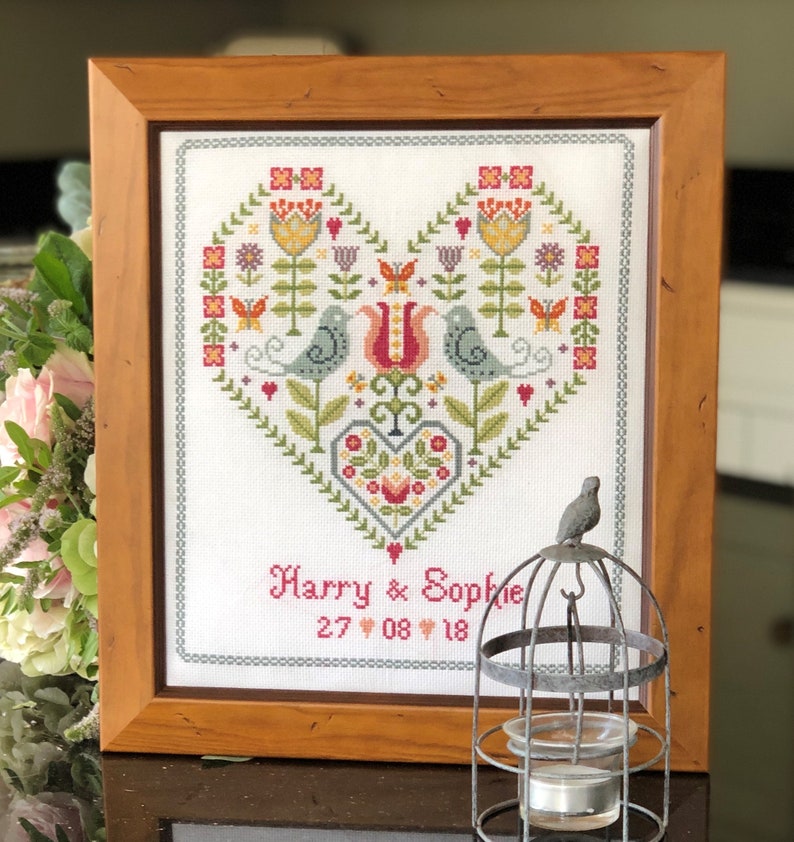 May include: A framed cross-stitch design featuring a heart with flowers, birds, and the text "Harry & Sophie 27 08 18".
