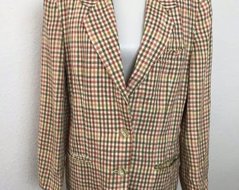 May include: A vintage blazer in a classic plaid pattern, featuring a mix of red, green, and beige squares. The blazer has a notched collar, two front pockets, and two buttons for closure. The garment is displayed on a mannequin.