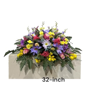 May include: A colorful floral arrangement featuring a variety of flowers in shades of yellow, pink, purple, and red. The arrangement is 32 inches wide and includes green foliage. The flowers are arranged on a rectangular base.