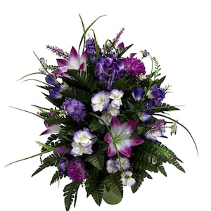 May include: A purple and white artificial flower arrangement in a green vase. The arrangement features lilies, hydrangeas, and other flowers.
