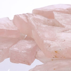 Pode incluir: Um monte de lascas de cristal de quartzo rosa. As lascas são de forma irregular e têm uma aparência translúcida.