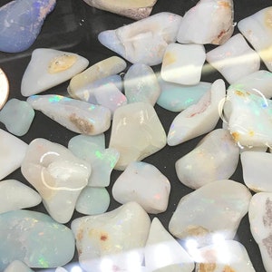 May include: A black bowl filled with water and a collection of white opal stones. The stones are various shapes and sizes, and some have a slight iridescent sheen.