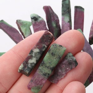 May include: A collection of green and pink gemstone chips. The chips are irregularly shaped and have a rough texture.
