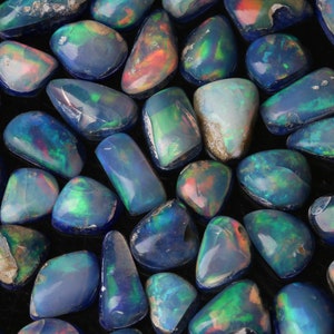 May include: A collection of iridescent blue and green opal gemstones, each with a unique shape and pattern. The stones are arranged in a circular pattern on a black background.