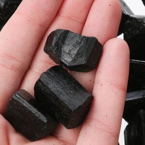 May include: A hand holding a collection of black tourmaline crystals. The crystals are rough and have a natural, unpolished look.