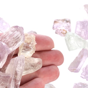 May include: A collection of small, translucent, pale pink and white crystals. The crystals are faceted and have a striated texture.