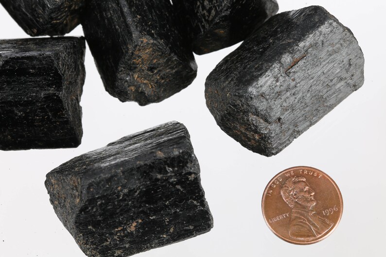 Może przedstawiać: Kolekcja czarnych kryształ&oacute;w turmalinu, niekt&oacute;re z lekkim połyskiem, obok amerykańskiego centa dla skali.