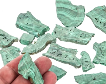 Op de afbeelding: Een verzameling gebroken stukken malachiet, een groene edelsteen, op een witte achtergrond. Sommige stukken bevinden zich in een hand.