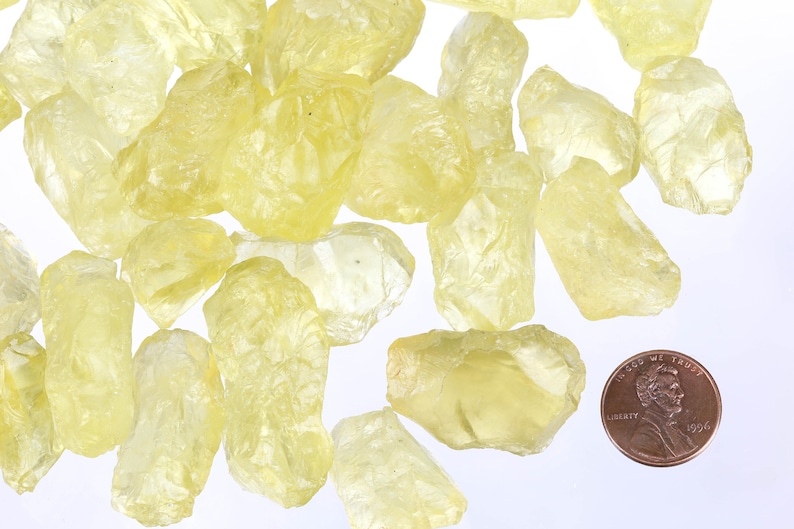 Puede incluir: Una colecci&oacute;n de cristales de citrino amarillo en bruto, algunos con una apariencia transl&uacute;cida, junto a un centavo de d&oacute;lar estadounidense para la escala.
