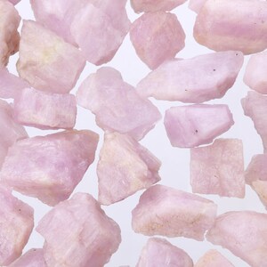 May include: A collection of pink and white rough gemstones. The stones are various sizes and shapes, and have a natural, unpolished look.