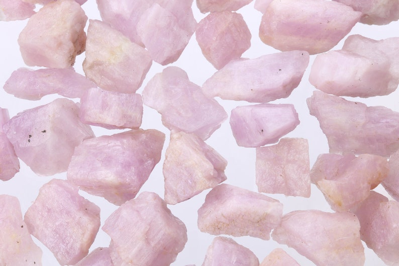 May include: A collection of pink and white rough gemstones. The stones are various sizes and shapes, and have a natural, unpolished look.