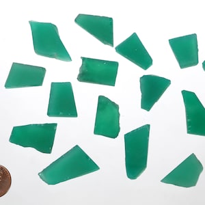May include: A collection of 15 green gemstone chips, some with a rectangular shape and others with a triangular shape. The chips are scattered on a white surface, with a US penny for scale.