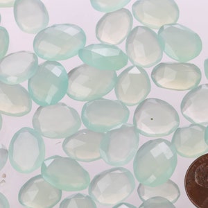 Puede incluir: Una colecci&oacute;n de virutas de piedra de calcedonia azul claro, algunas con un ligero tono verde, en varios tama&ntilde;os y formas. Las virutas est&aacute;n dispuestas sobre una superficie blanca.