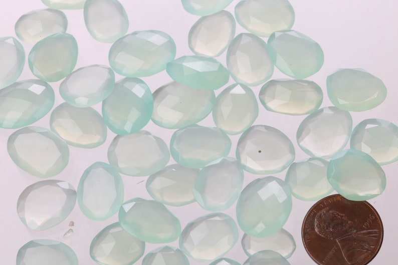 Puede incluir: Una colecci&oacute;n de virutas de piedra de calcedonia azul claro, algunas con un ligero tono verde, en varios tama&ntilde;os y formas. Las virutas est&aacute;n dispuestas sobre una superficie blanca.