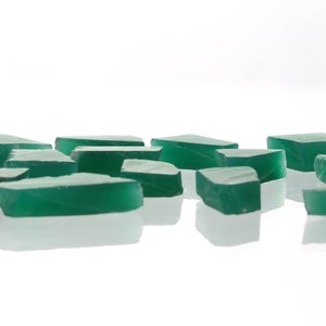 May include: A collection of green, irregularly shaped, translucent glass pieces. The pieces are scattered on a white surface.