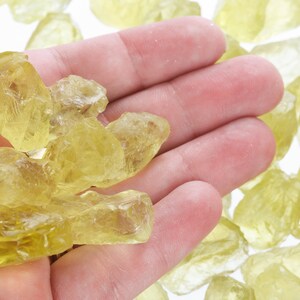 Pu&ograve; includere: Una mano che tiene un mucchio di cristalli di citrino gialli. I cristalli sono di varie dimensioni e forme, e sono tutti traslucidi.