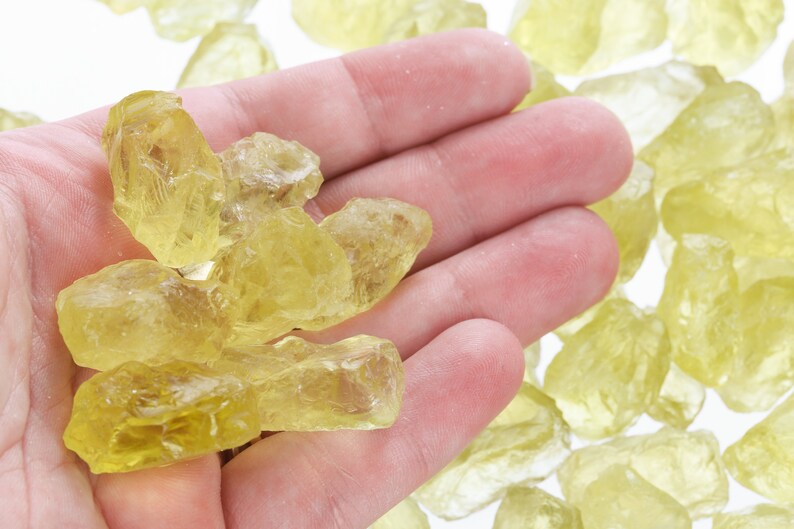 Pu&ograve; includere: Una mano che tiene un mucchio di cristalli di citrino gialli. I cristalli sono di varie dimensioni e forme, e sono tutti traslucidi.