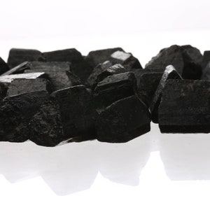 May include: A pile of black obsidian crystals, also known as black volcanic glass, on a white background.