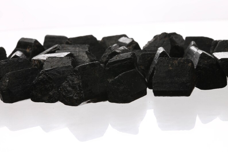 May include: A pile of black obsidian crystals, also known as black volcanic glass, on a white background.