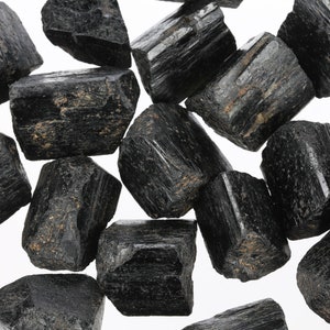 Może przedstawiać: Kolekcja czarnych kryształ&oacute;w turmalinu, znanych r&oacute;wnież jako szorl, o surowym, naturalnym wykończeniu. Kryształy mają r&oacute;żne rozmiary i kształty, niekt&oacute;re z nich wykazują prążkowanie i fasetki.