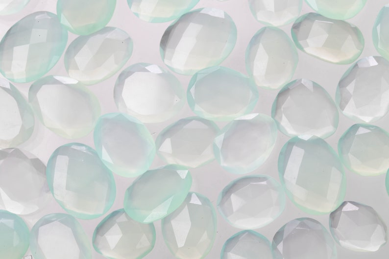 Puede incluir: Una colecci&oacute;n de piedras preciosas ovaladas facetadas de color verde p&aacute;lido. Las piedras est&aacute;n dispuestas en un patr&oacute;n aleatorio sobre un fondo blanco.