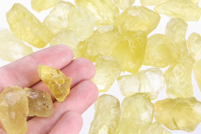 Puede incluir: Una colecci&oacute;n de cristales de citrino amarillo, algunos de los cuales est&aacute;n en una mano. Los cristales son &aacute;speros y tienen un aspecto natural sin pulir.