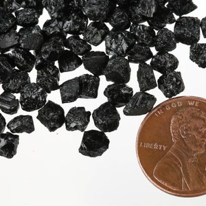 May include: A pile of black, rough, and jagged black tourmaline crystals next to a US penny for scale.  The crystals are about the size of a penny.