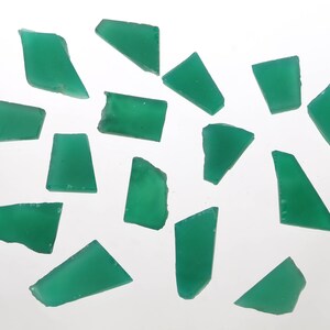 May include: A collection of 15 green gemstone chips, each with a unique irregular shape. The chips are scattered on a white surface.