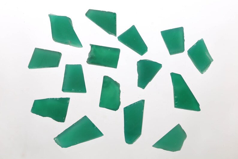 May include: A collection of 15 green gemstone chips, each with a unique irregular shape. The chips are scattered on a white surface.