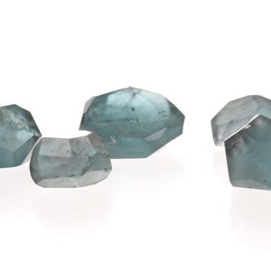 May include: Four faceted, light blue gemstones with a slightly cloudy appearance.