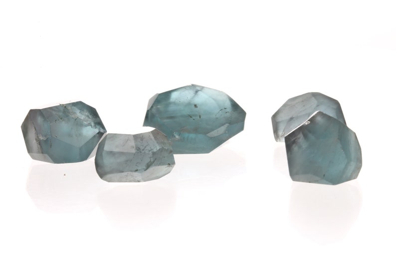 May include: Four faceted, light blue gemstones with a slightly cloudy appearance.
