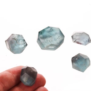 May include: Five blue-green faceted crystals of various sizes. The crystals are translucent and have a slight shimmer.