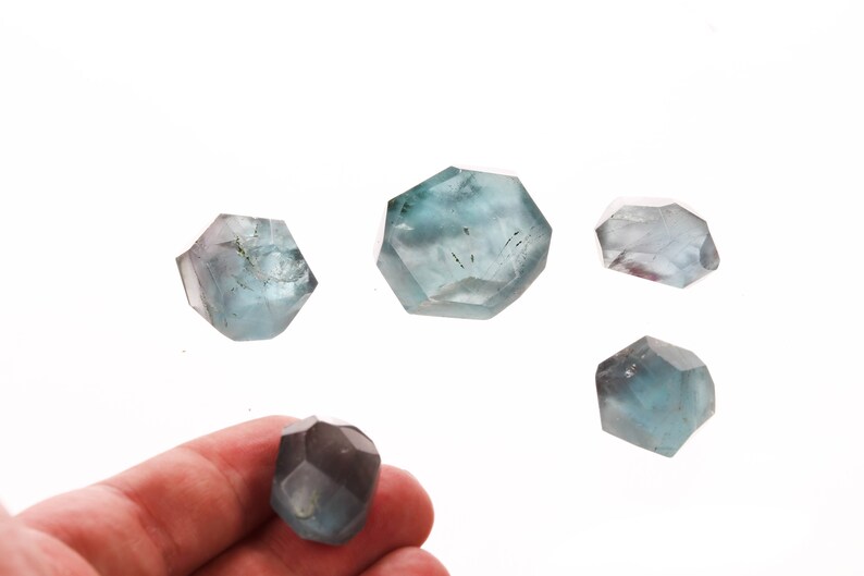 May include: Five blue-green faceted crystals of various sizes. The crystals are translucent and have a slight shimmer.