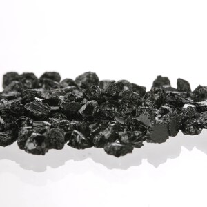 May include: A pile of black, rough, and irregularly shaped crystals on a white background.