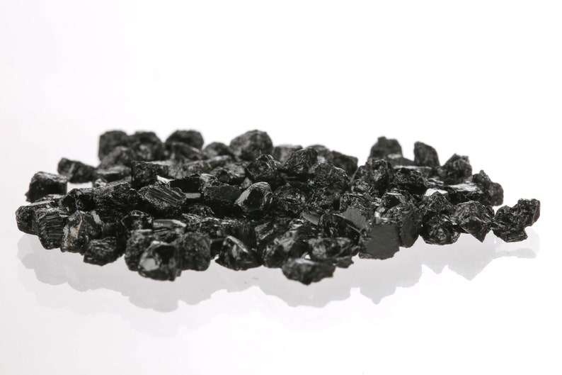 May include: A pile of black, rough, and irregularly shaped crystals on a white background.