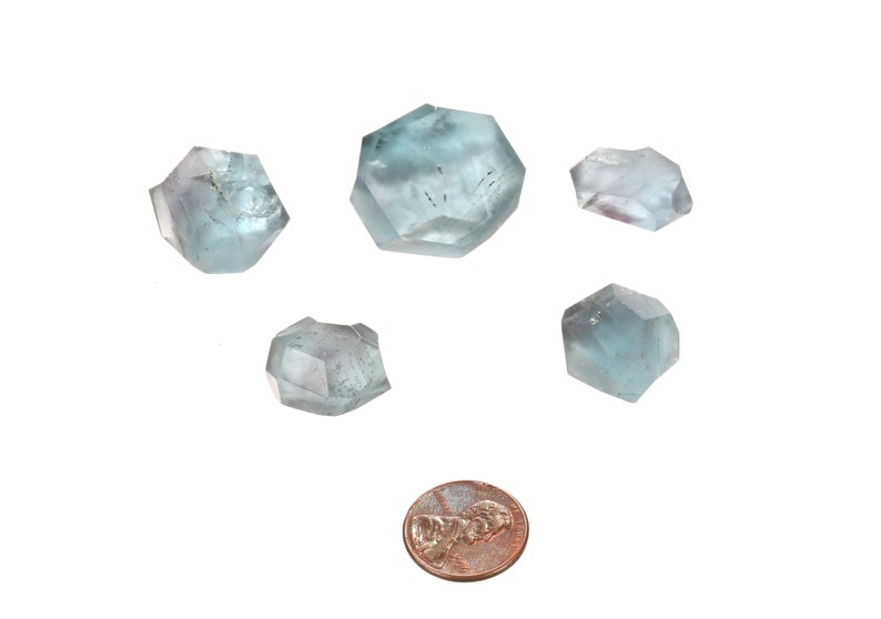 May include: Six light blue aquamarine crystals of varying sizes, with a penny for scale.