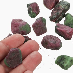 May include: A collection of green and pink rough gemstones. The stones are various sizes and shapes.