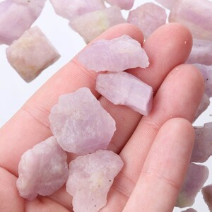 May include: A collection of pale pink and purple rough gemstones. The stones are various shapes and sizes and have a translucent appearance.