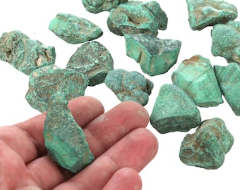 Op de afbeelding: Een verzameling ruwe, groene malachietstenen. De stenen zijn van verschillende groottes en vormen, sommige hebben een meer kristallijne textuur.