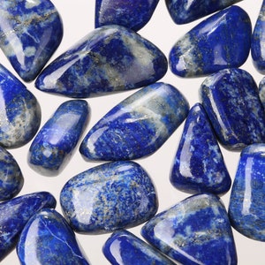 May include: A collection of tumbled lapis lazuli stones. The stones are a deep blue color with white and gold flecks. They are smooth and polished.