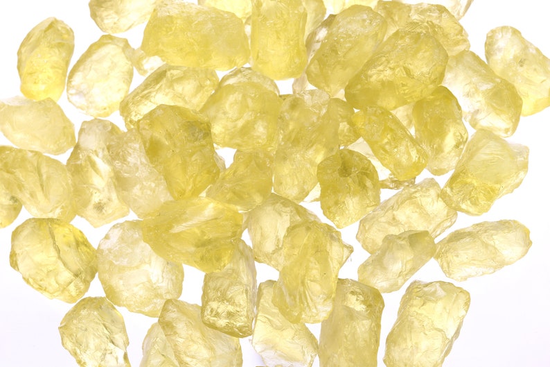 Pu&ograve; includere: Una collezione di cristalli gialli, traslucidi, tagliati grezzi. I cristalli sono di varie dimensioni e forme, e sono sparsi su uno sfondo bianco.