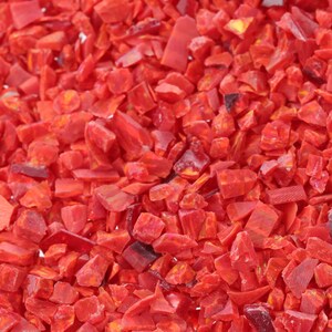 May include: A close-up view of a pile of small, red, irregular-shaped pieces of crushed red glass. The pieces are various sizes and shapes, and they are all a vibrant red color.