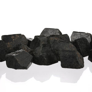 Może przedstawiać: Grupa czarnych, szorstkich i nieregularnych kryształ&oacute;w. Kryształy są zgrupowane na białym tle.