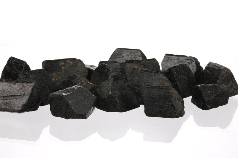 Może przedstawiać: Grupa czarnych, szorstkich i nieregularnych kryształ&oacute;w. Kryształy są zgrupowane na białym tle.