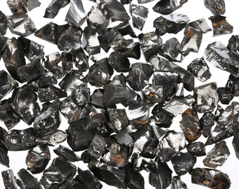 Könnte beinhalten: Eine Sammlung schwarzer Obsidian-Steine, einige mit einem leichten irisierenden Schimmer, verstreut auf weißem Hintergrund.