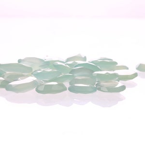 Puede incluir: Un mont&oacute;n de piedras preciosas ovaladas transl&uacute;cidas de color verde claro sobre una superficie blanca.