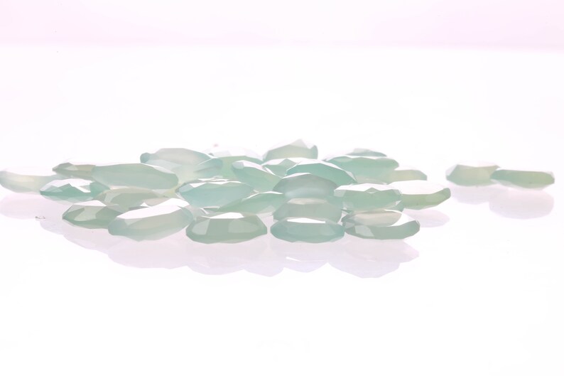 Puede incluir: Un mont&oacute;n de piedras preciosas ovaladas transl&uacute;cidas de color verde claro sobre una superficie blanca.