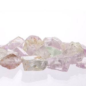 May include: A collection of pale pink, white, and green crystals with a variety of shapes and sizes. The crystals are arranged in a pile on a white surface.