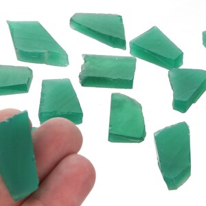 May include: A collection of green glass pieces, some are rectangular, some are triangular, and some are irregular shapes. The glass pieces are translucent and have a slight shimmer.